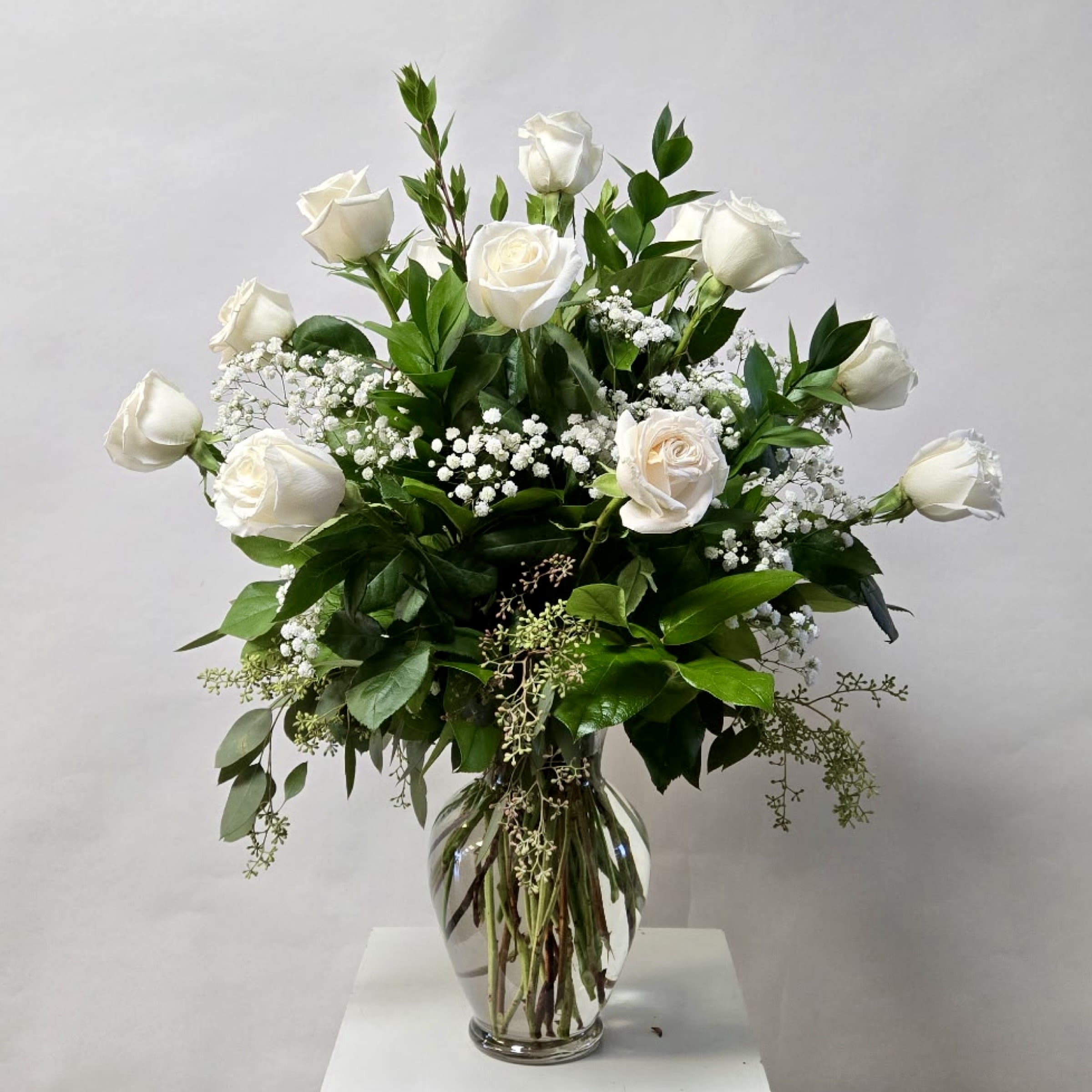 White roses in a clear glass vase with baby's breath and greenery