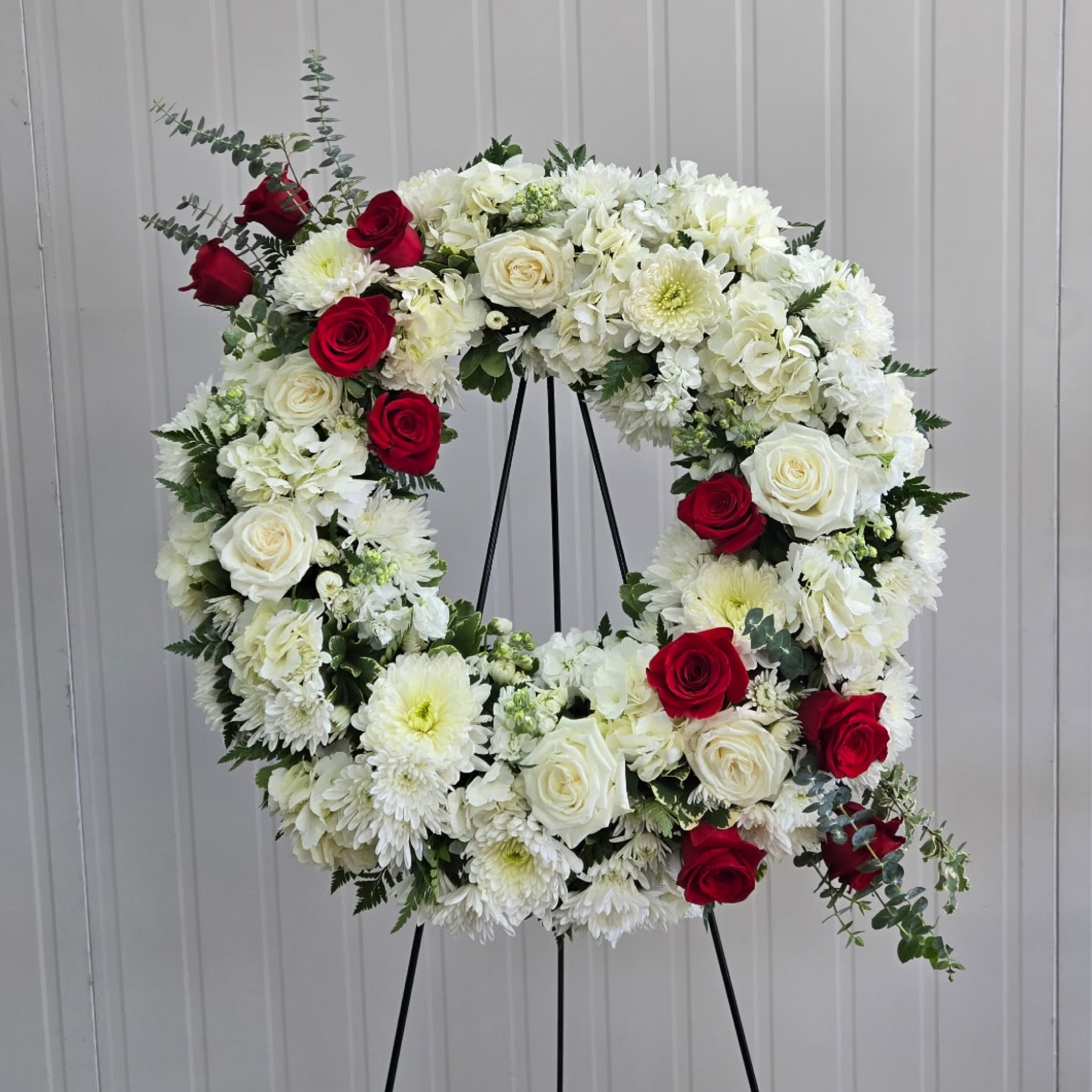 Tribute Wreath - This 18" Wreath on an Easel includes, White Hydrangea, White Fuji Mums, White and Red Roses, White Stock, White Cushion Mums, Mini White Carnations and Red Spray Roses. Or as Similar as Possible. 