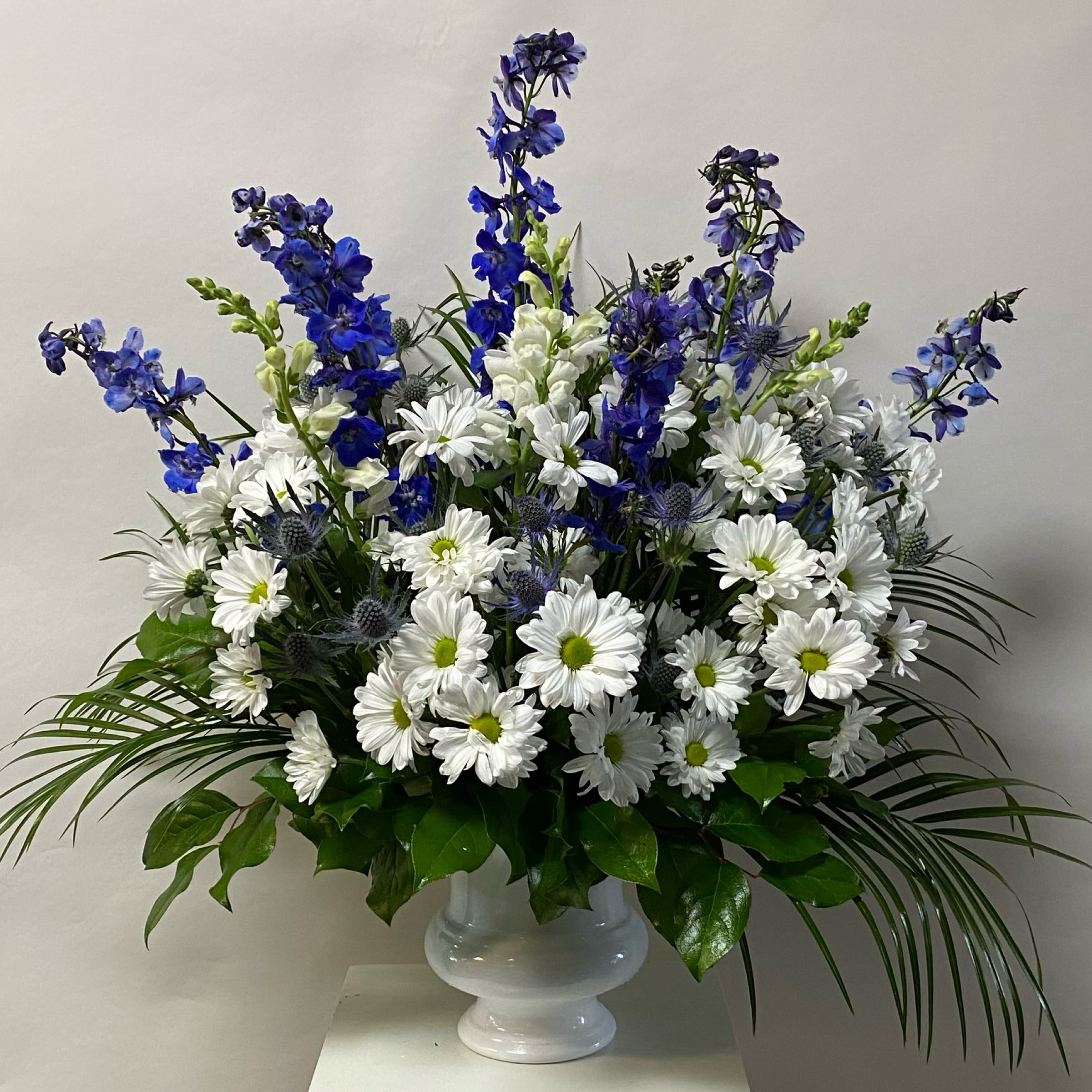 Ocean Song Arrangement - This Arrangement Includes Blue Delphinium, White Snapdragons, Blue Thistle and White Daisies in a Mortuary Approved white Plastic Container. Or as Similar as Possible. 