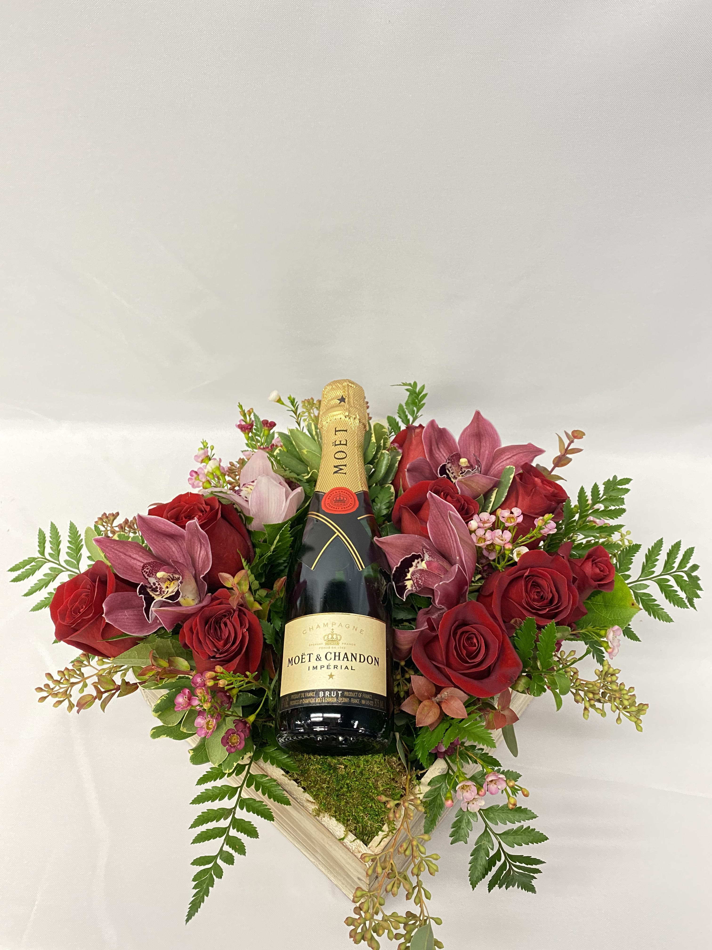 Red roses and pink orchids arranged around a champagne bottle