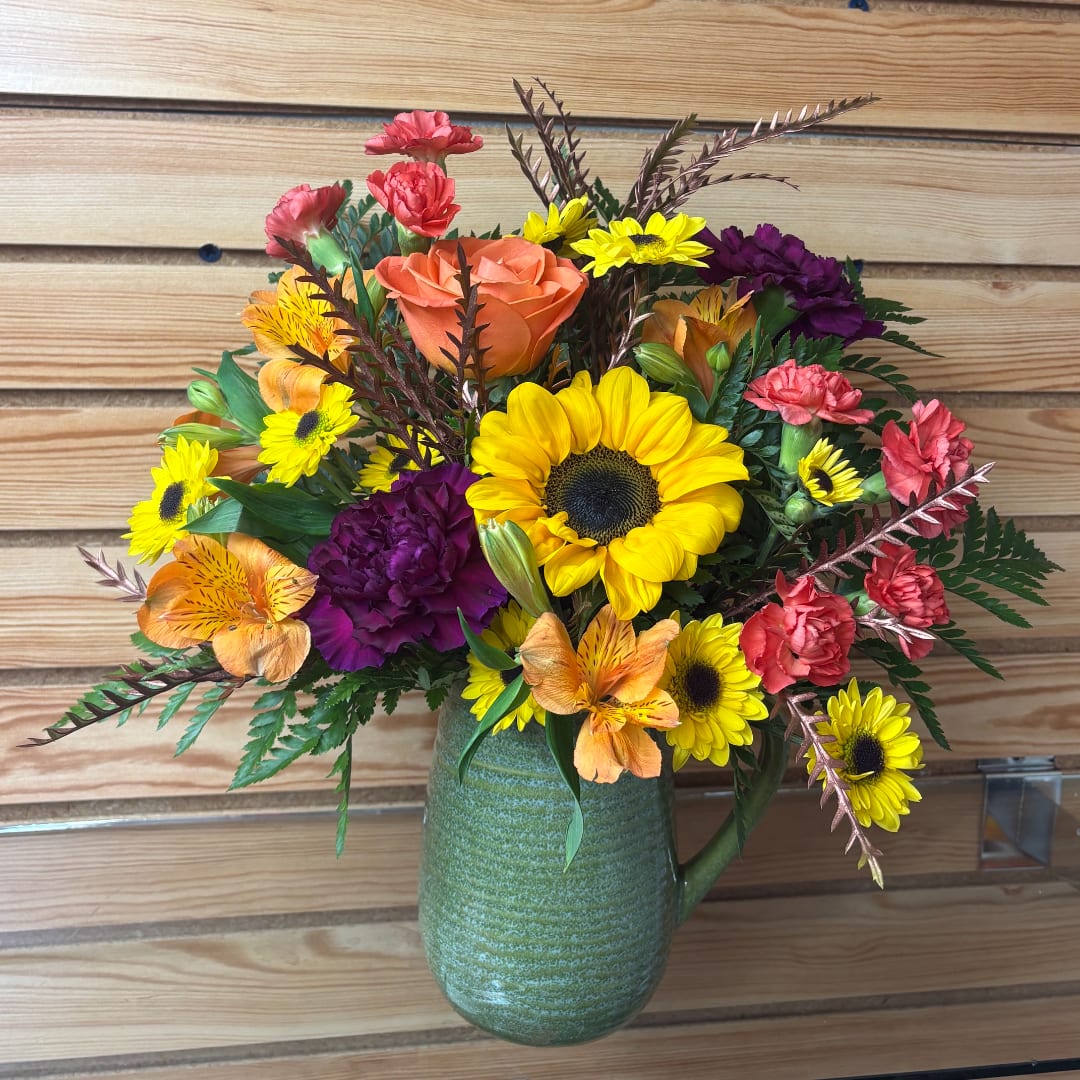 Mixed bouquet of sunflowers, roses, carnations, and alstroemeria in a green vase