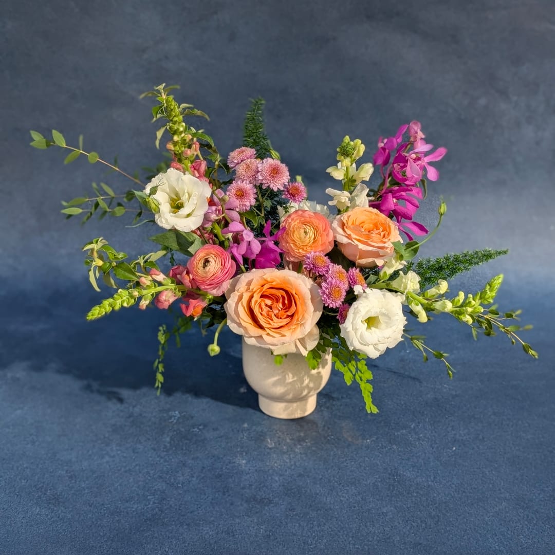 Mixed bouquet of peach, white, and pink flowers in a white vase