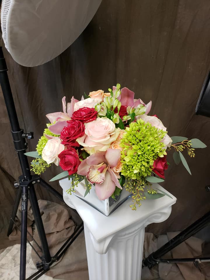 Bouquet of pink and red roses with orchids and green blooms in a white vase