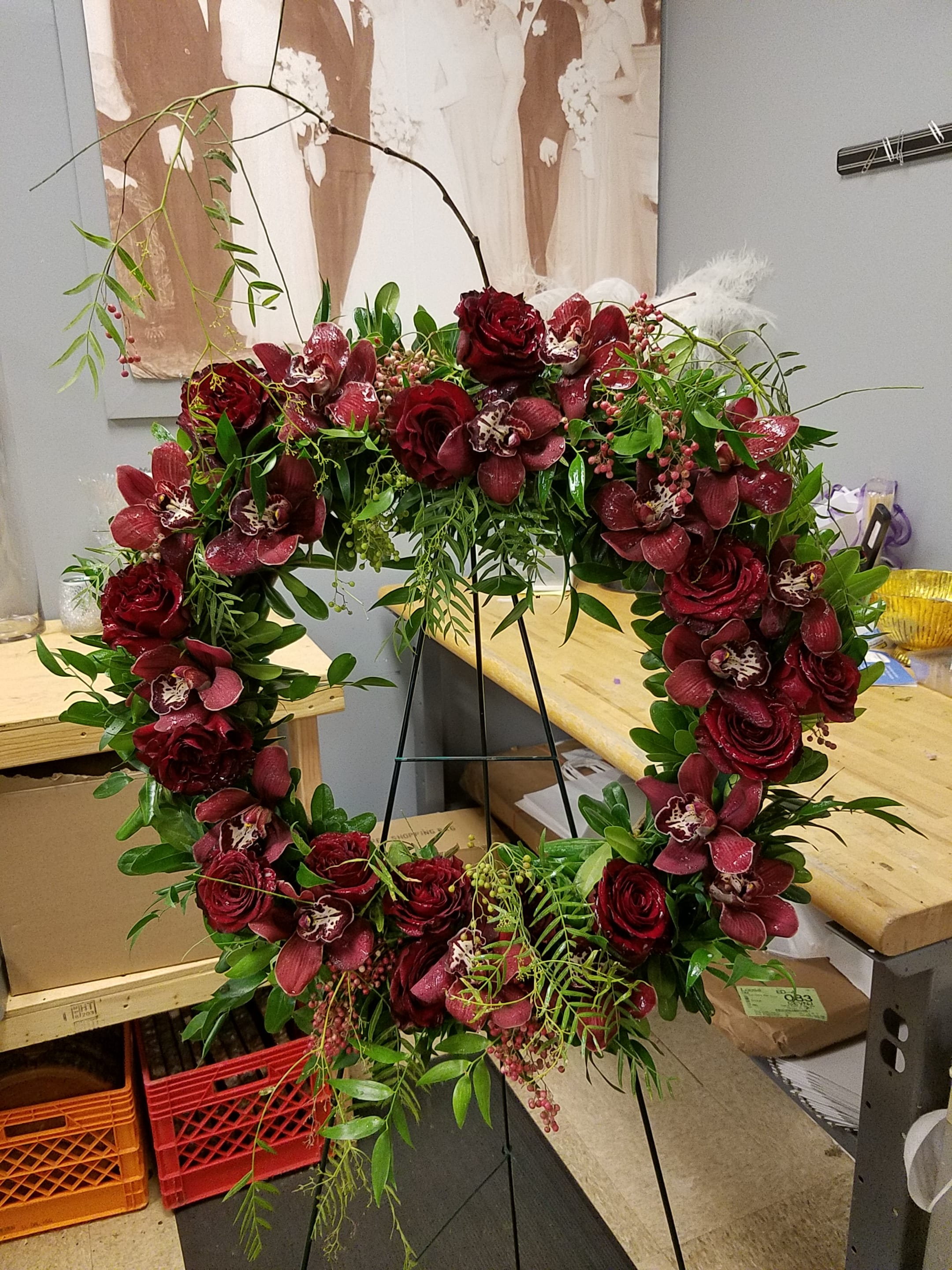 Heart-shaped floral wreath with deep red roses and orchids on a stand