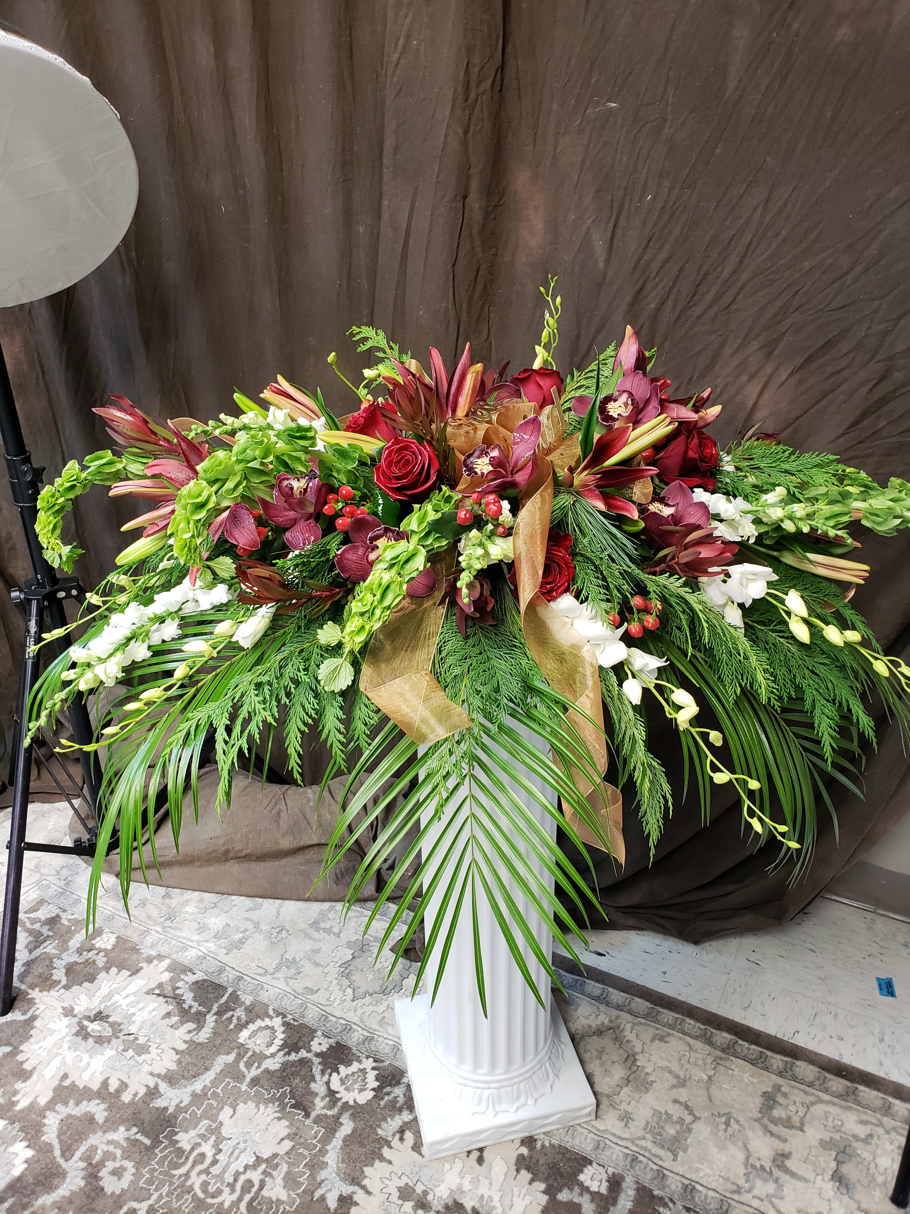 Large floral spray with red roses, burgundy orchids, and white blooms on a pedestal