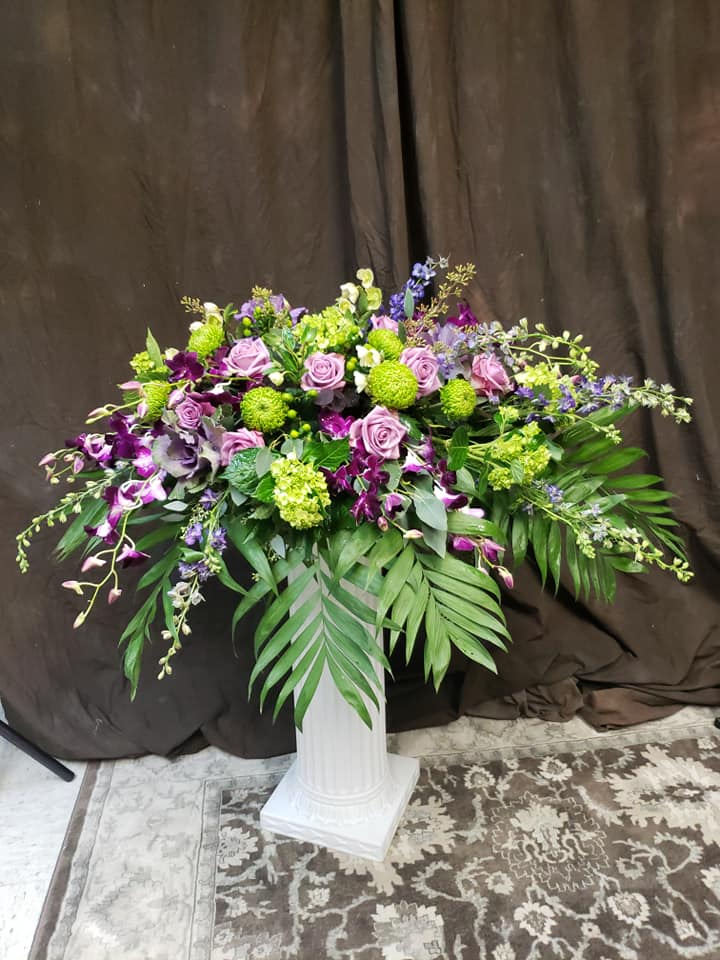 Large floral arrangement with purple and green flowers in a white pedestal vase