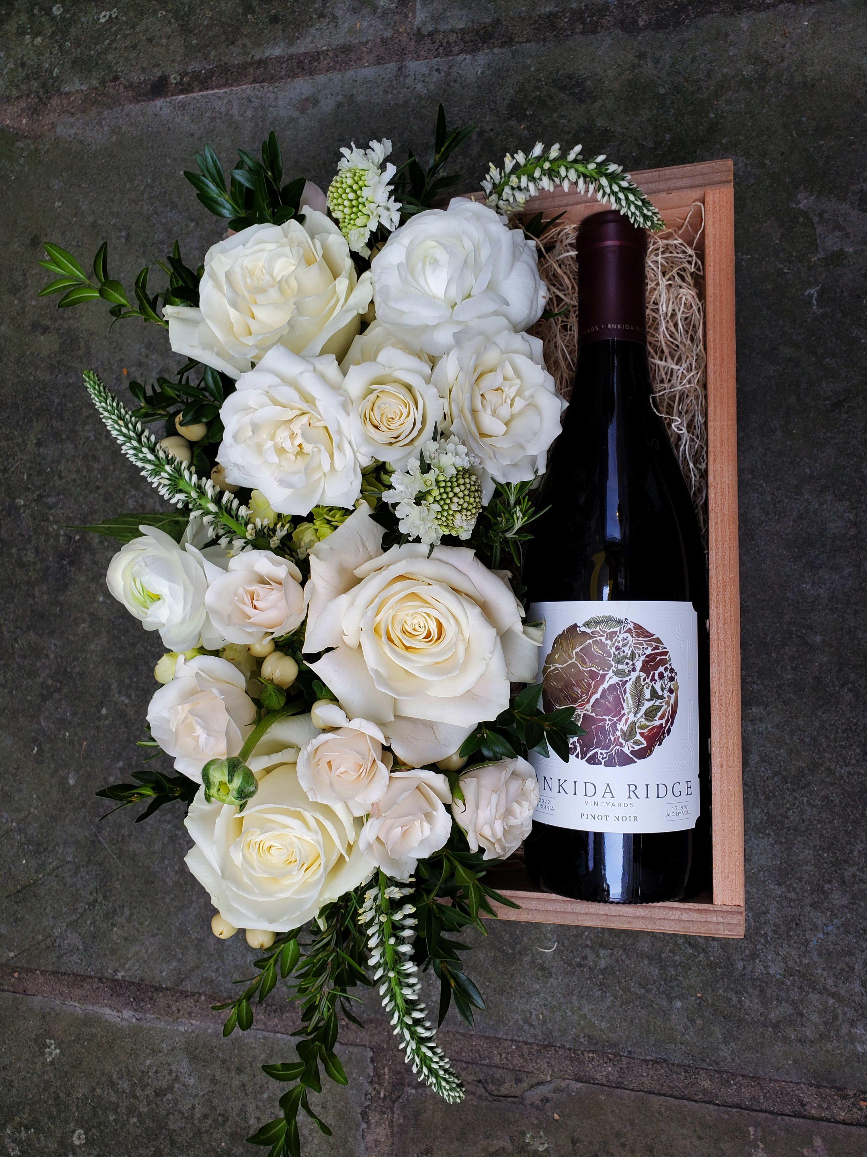 White rose arrangement in a wooden box with a wine bottle