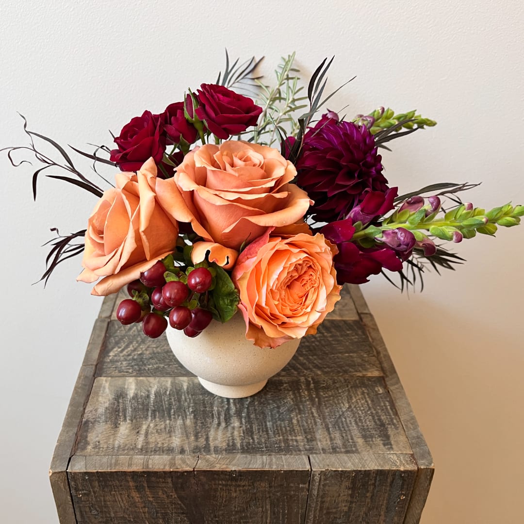 Peach and burgundy roses arranged in a white vase