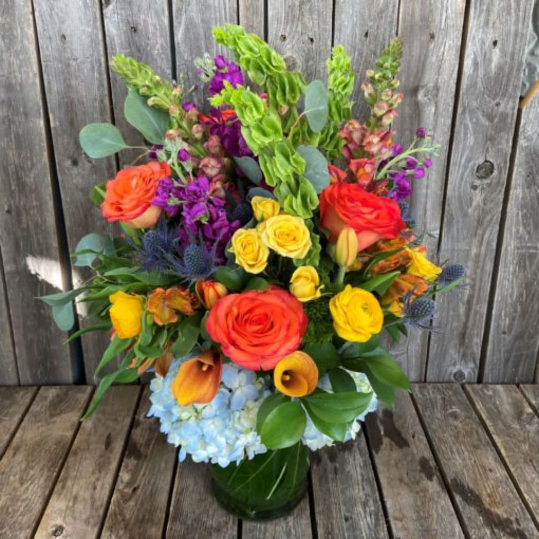 Colorful mixed bouquet with roses, calla lilies, and blue hydrangea in a green vase