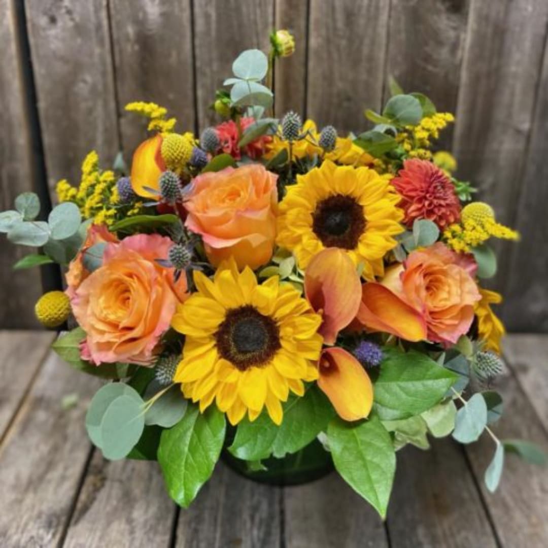 Bouquet of sunflowers, peach roses, and orange calla lilies in a low vase