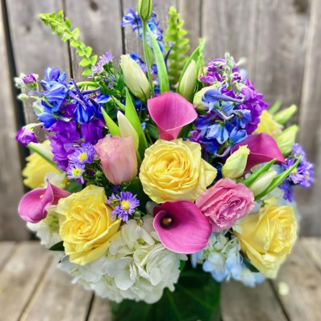 Colorful bouquet with yellow roses, pink calla lilies, and blue-purple flowers in a vase
