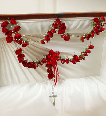 Red rose garlands with bow and rosary cross draped inside a white lined casket lid