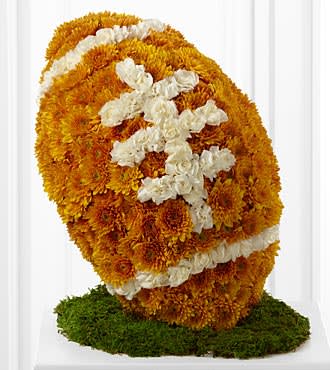 Football-shaped arrangement of orange flowers with white accents on a green moss base