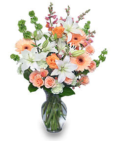 Tall bouquet of white lilies and peach roses with gerberas and snapdragons in a clear glass vase
