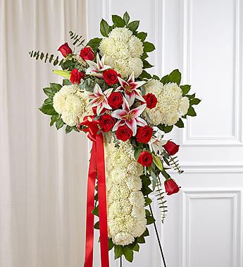 Standing floral cross with red roses and white blooms on a ribboned easel