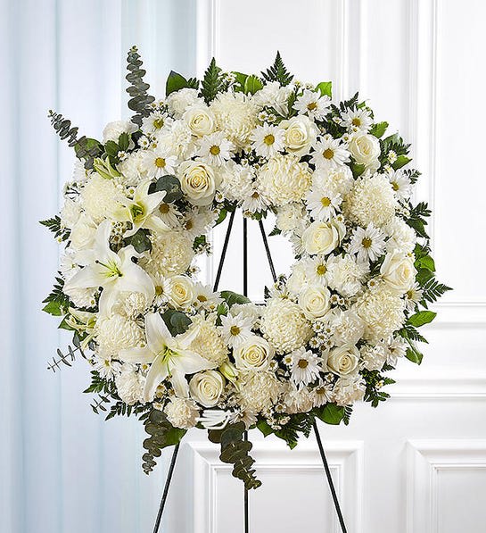 White floral wreath on a black stand with roses and daisies