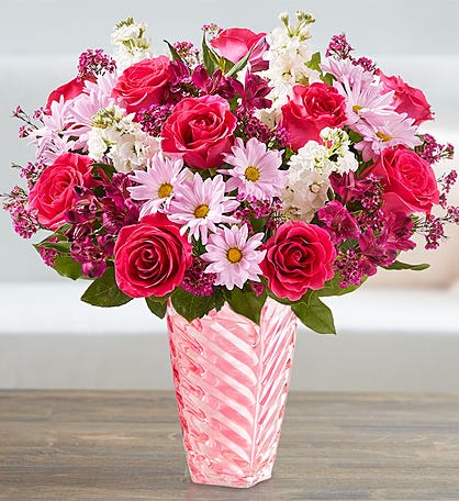 Pink and white mixed bouquet with roses and daisies in a tall pink glass vase