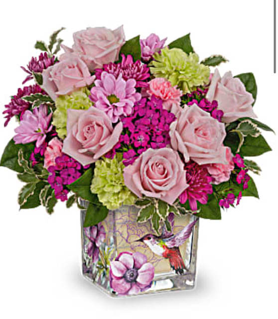 Compact arrangement of pink roses and bright blooms in a square glass vase with a hummingbird design