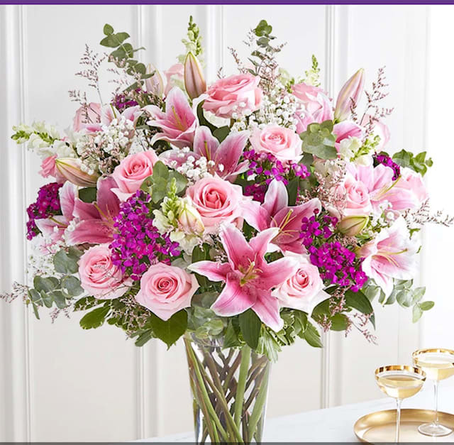 Tall arrangement of pink roses and lilies with bright fuchsia blooms in a clear glass vase