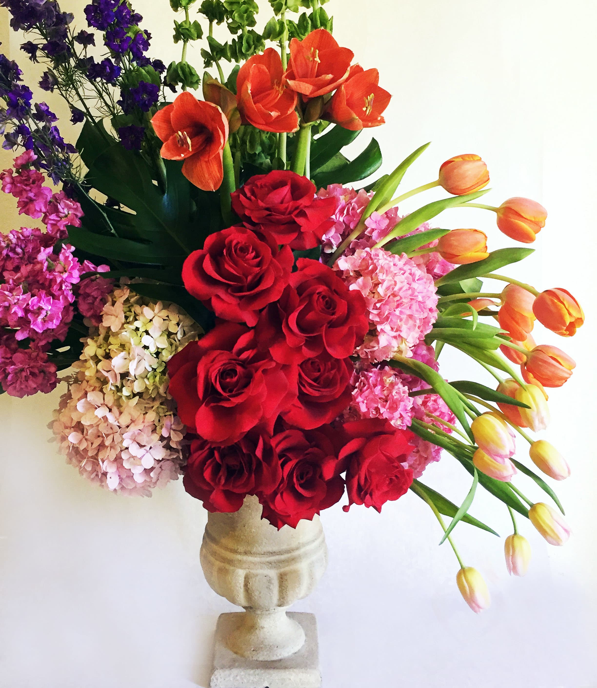 Mixed bouquet of red roses, orange tulips, and pink hydrangeas in a stone vase