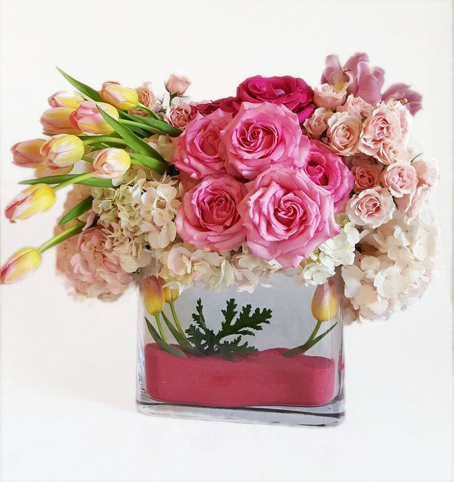Pink roses and tulips arranged in a clear rectangular vase