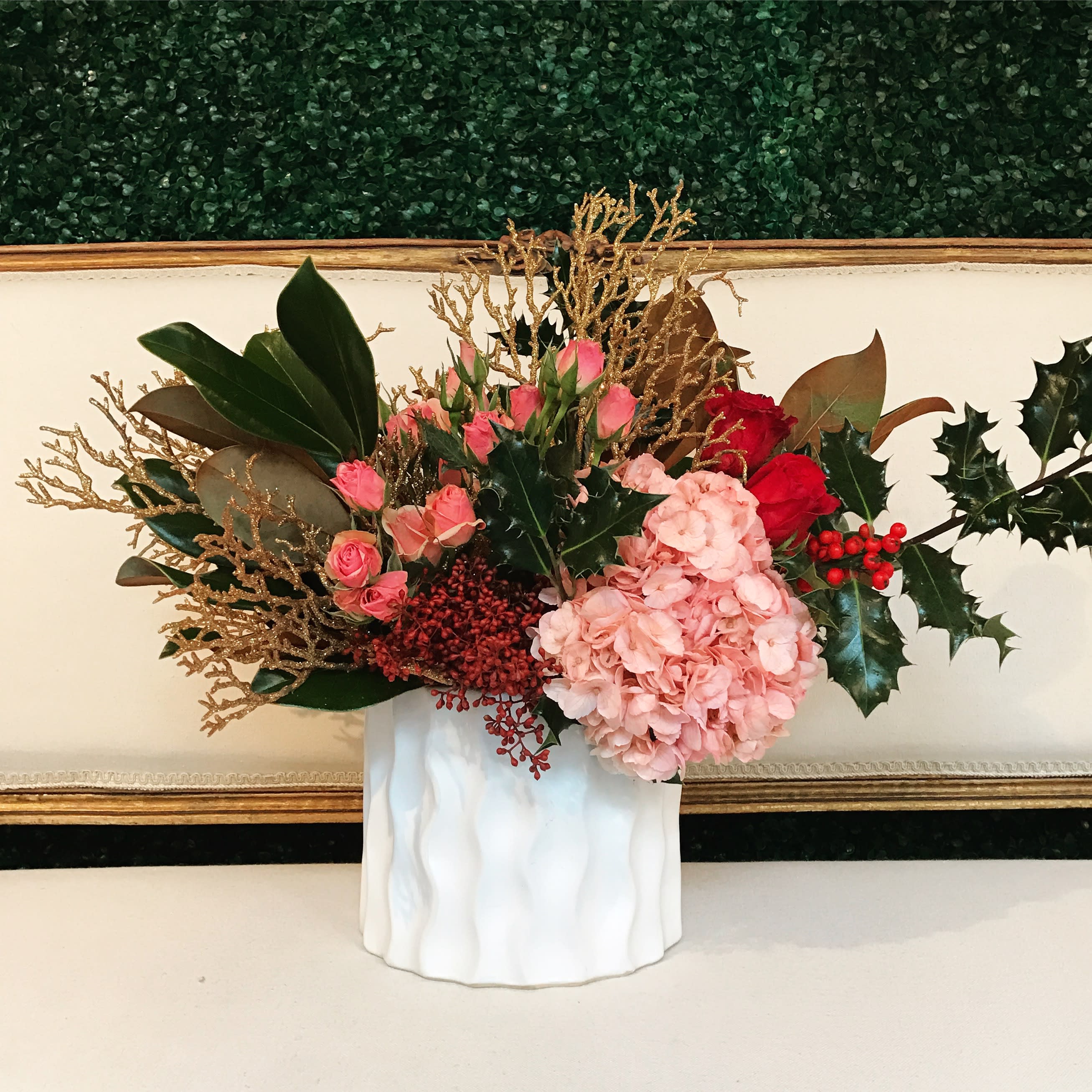 Pink flowers and red berries arranged in a white vase with gold branches