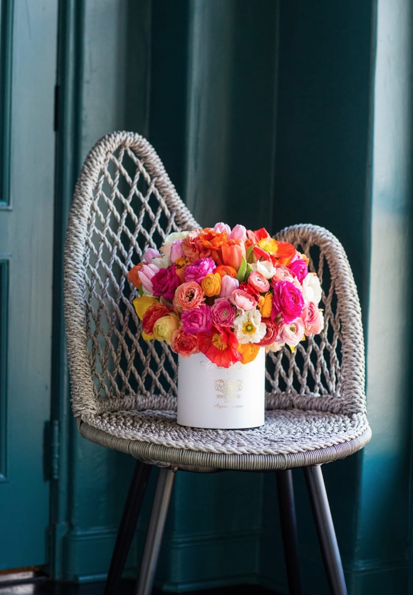 Bright mixed bouquet in a white cylindrical box on a woven chair
