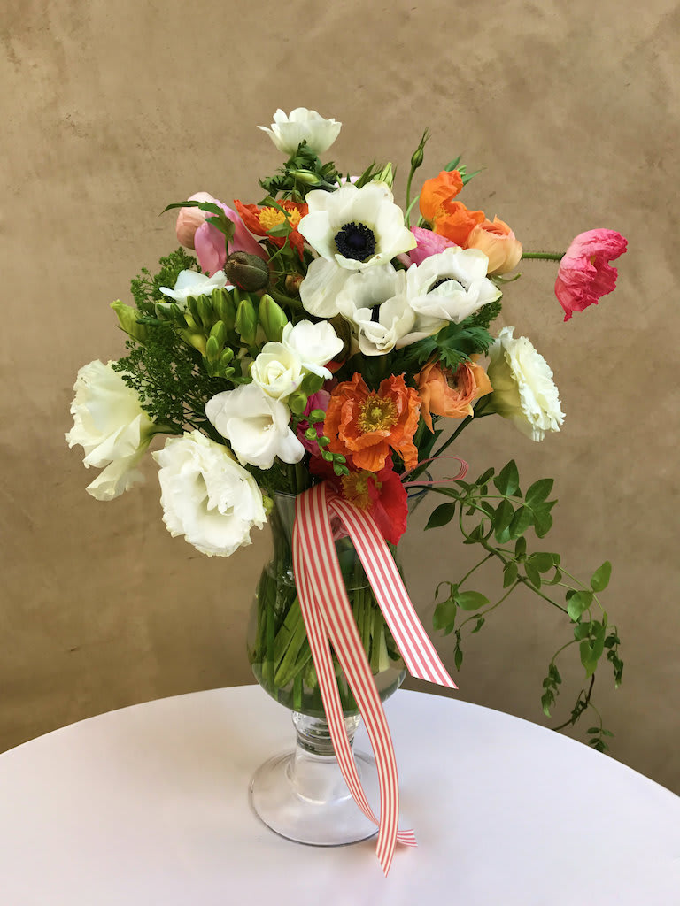 Mixed bouquet of white, orange, and pink flowers in a glass vase with a striped ribbon