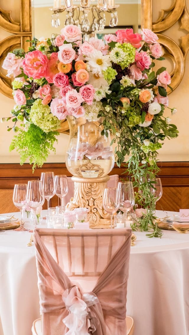 Large pink and white floral centerpiece in a clear vase on a decorated table