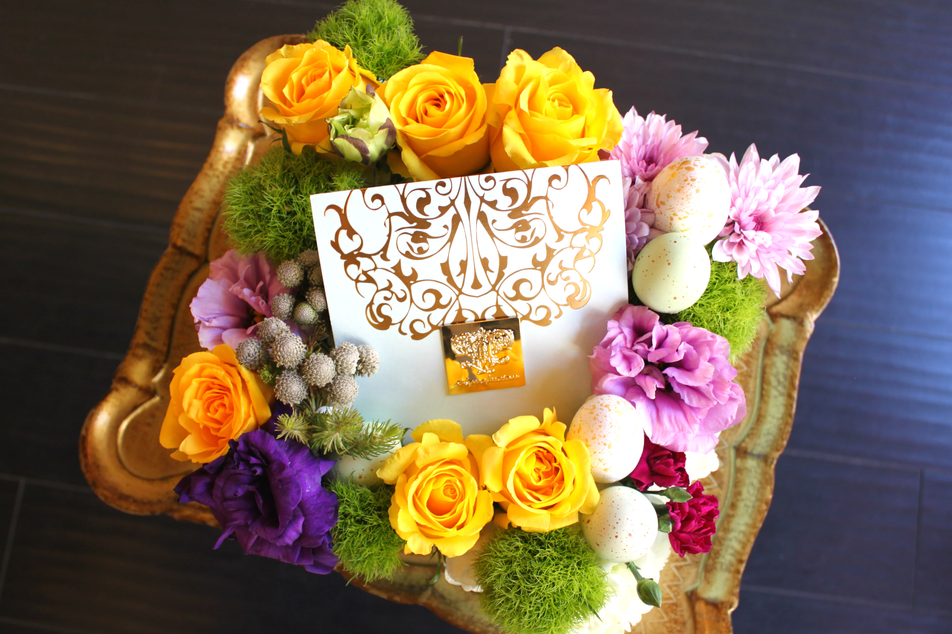 Floral gift arrangement with yellow roses, purple blooms, and decorative eggs in a tray