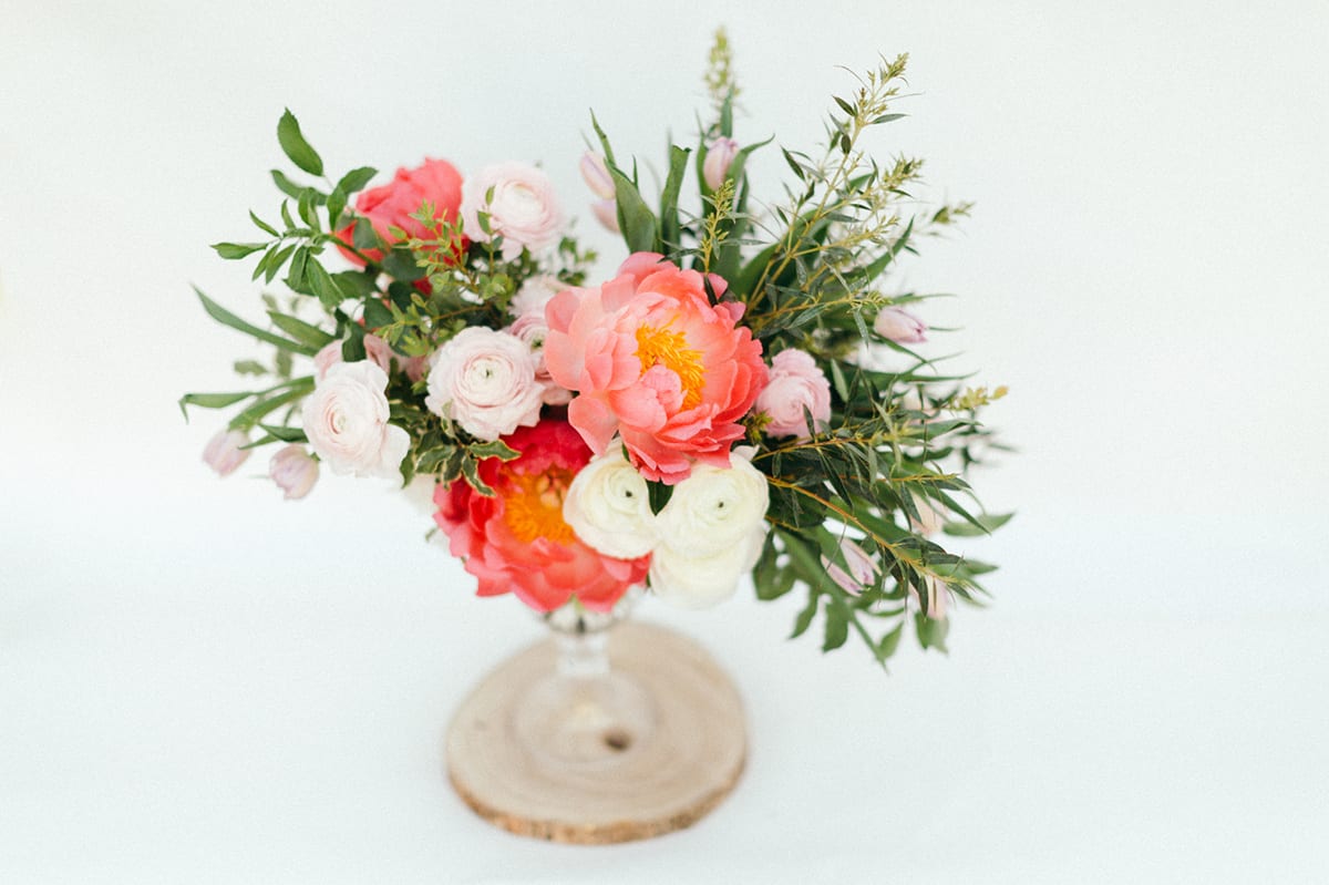 Pink and white floral arrangement in a clear vase on a wood slice base