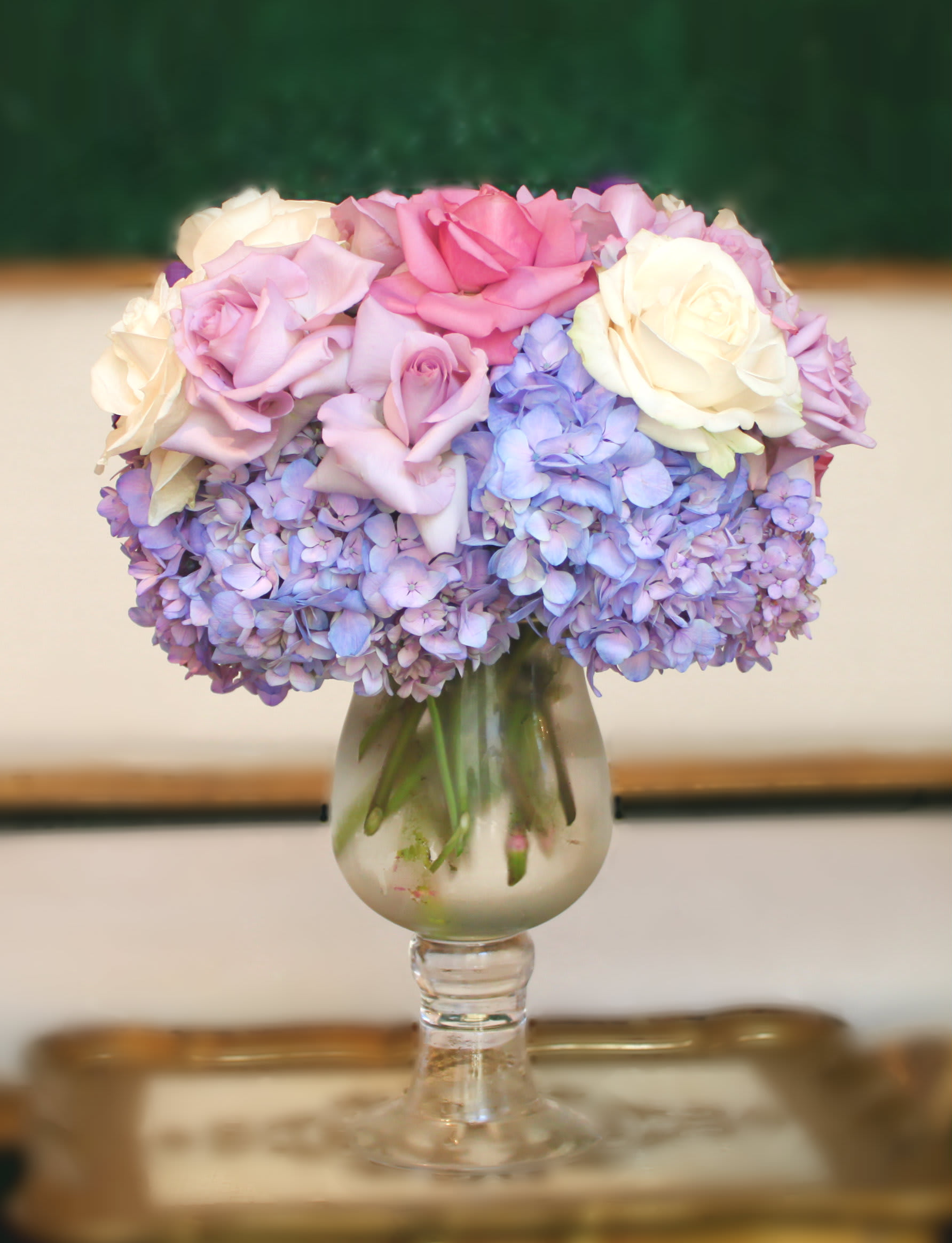 Pink and white roses arranged with lavender hydrangeas in a glass vase