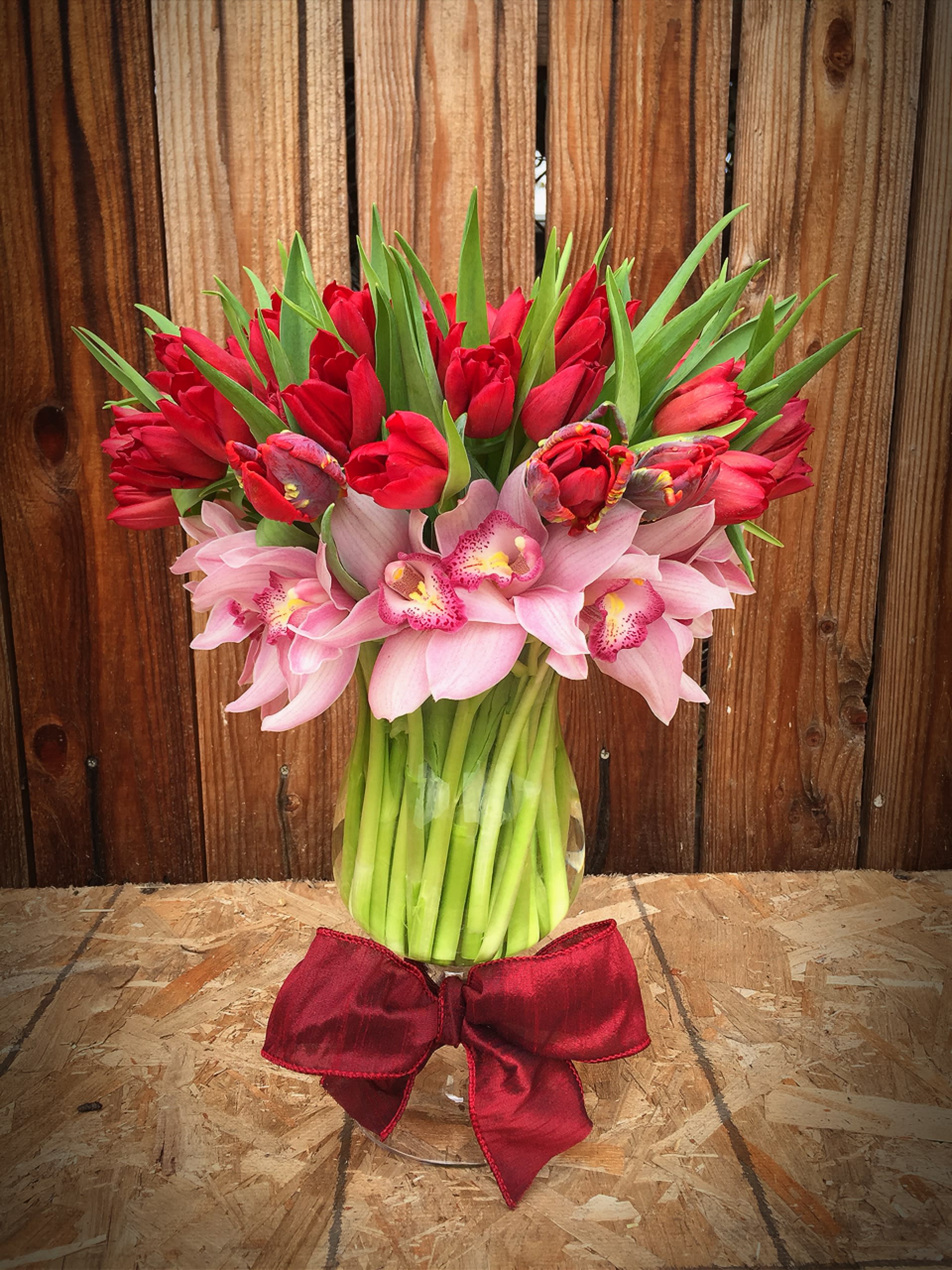 Bouquet of red tulips and pink orchids in a glass vase with a red bow