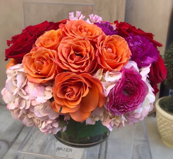 Round bouquet of orange, red, pink, and purple flowers in a glass vase
