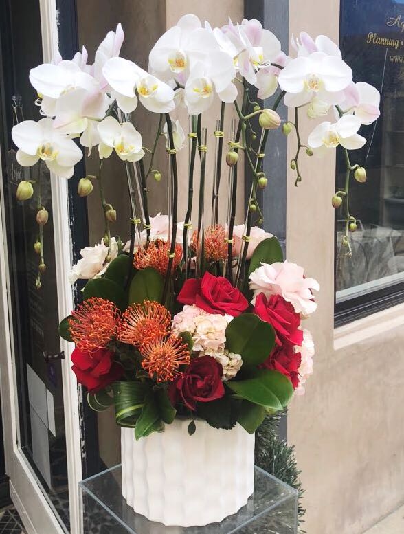Tall floral arrangement with white orchids and red roses in a white vase