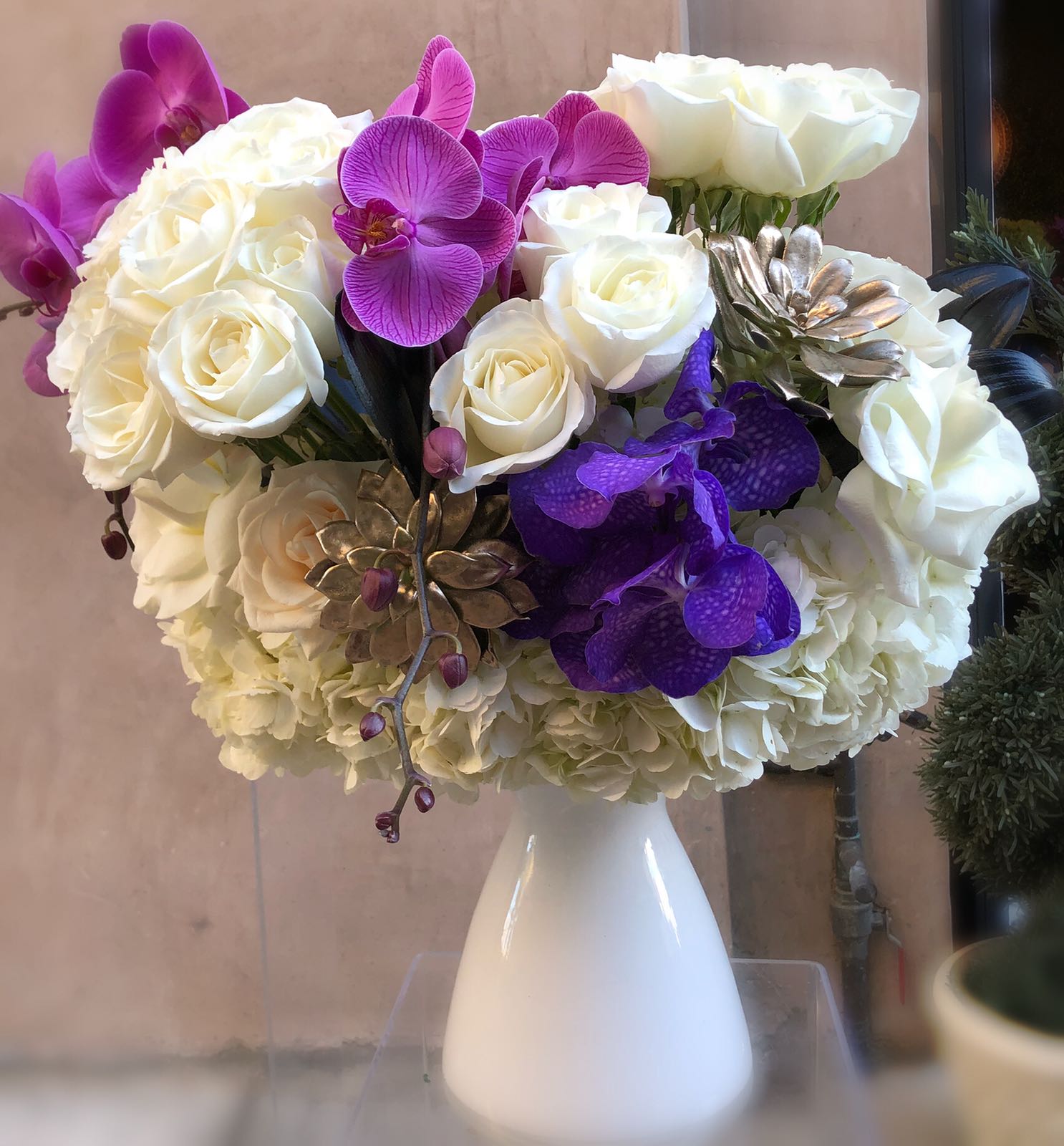 White roses and purple orchids arranged in a white vase