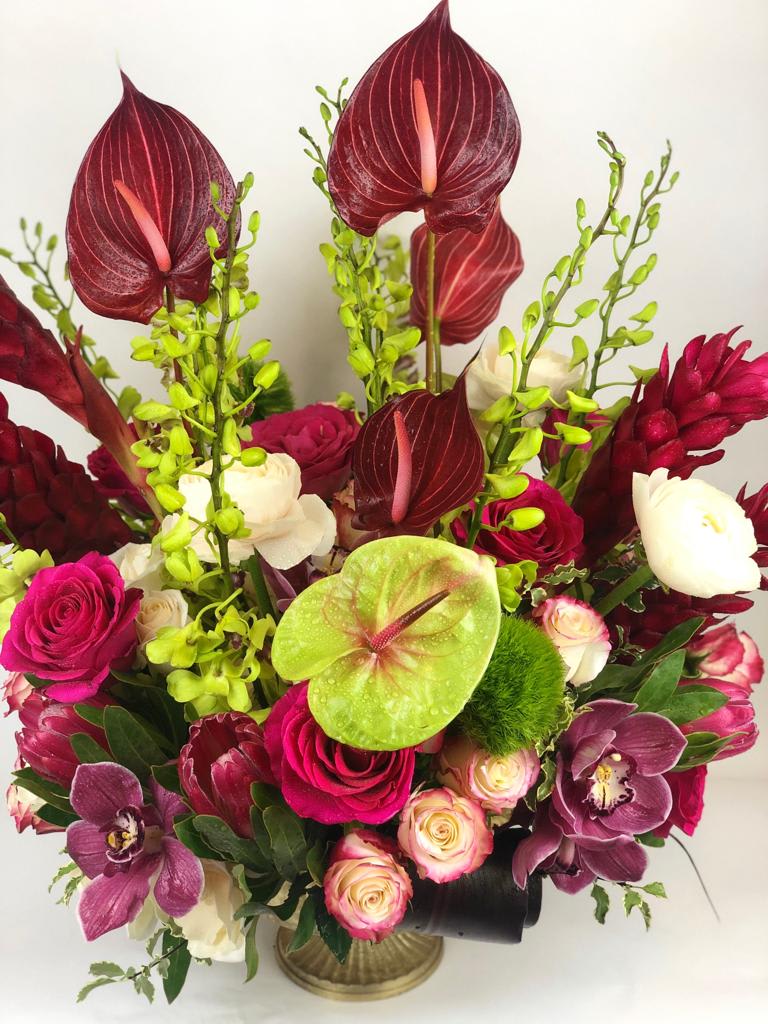 Tropical bouquet with burgundy anthuriums, roses, and orchids in a vase