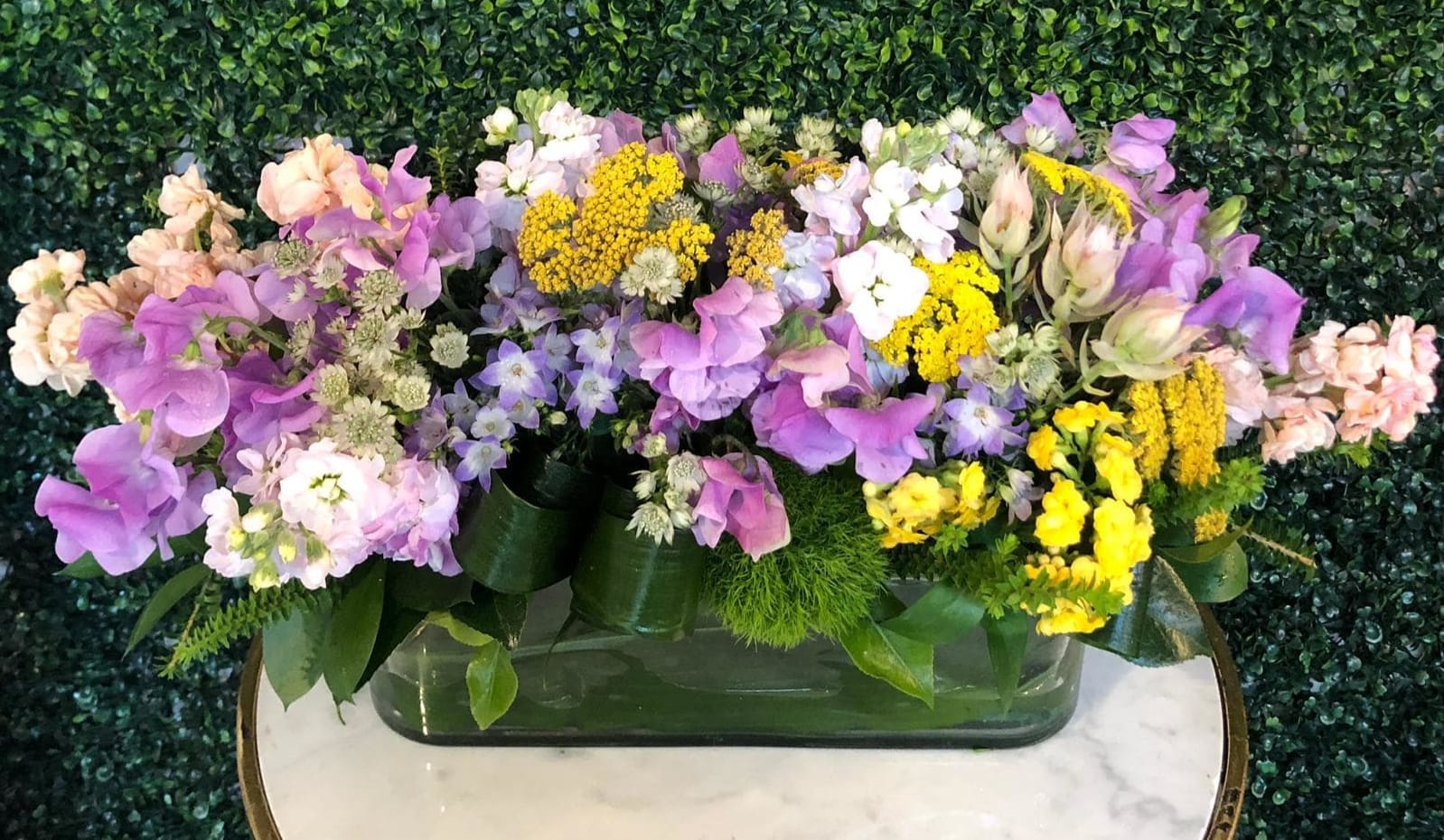 Mixed bouquet of purple, pink, white, and yellow flowers in a low rectangular vase