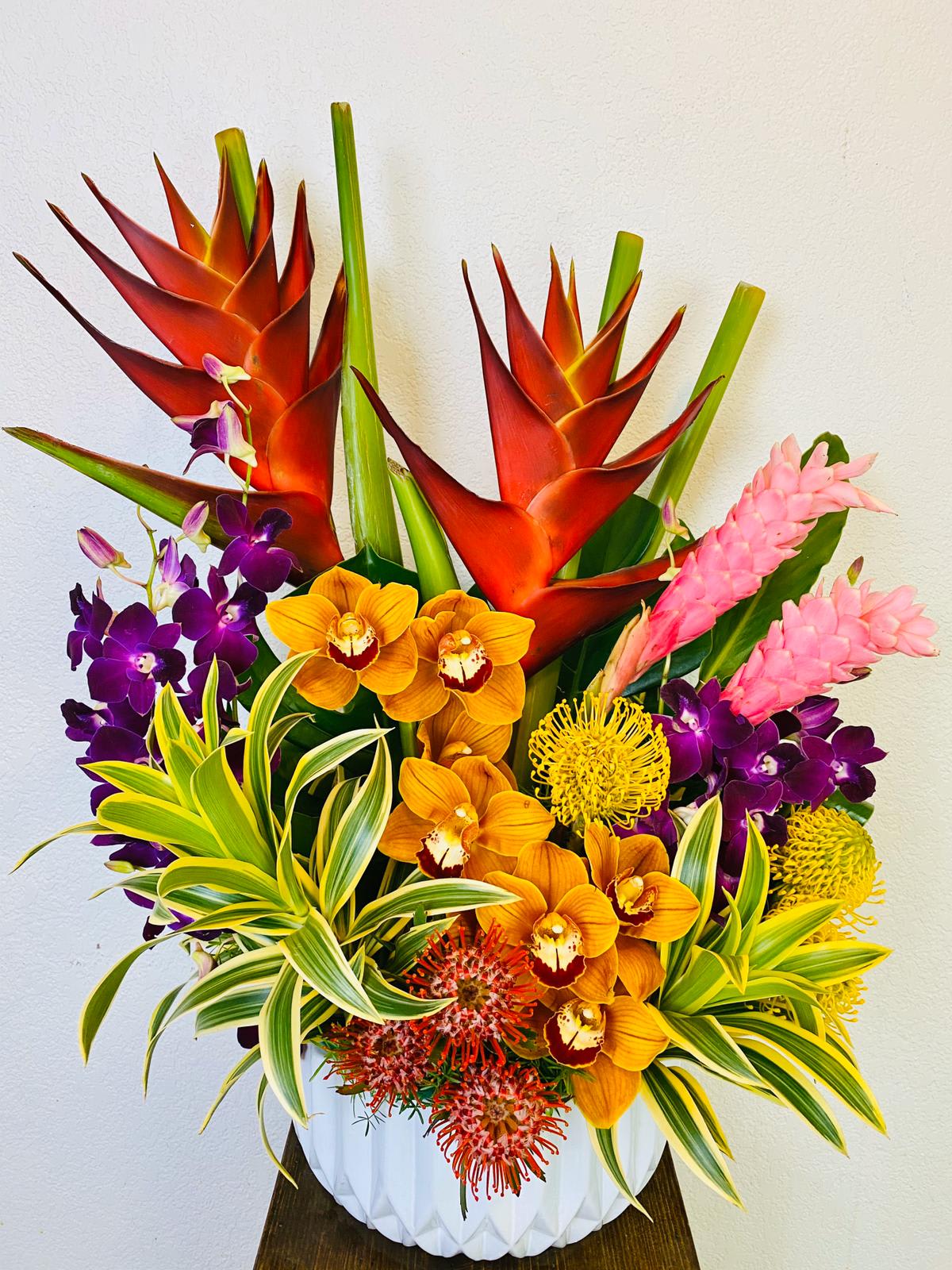 Tropical arrangement with orange heliconia, orchids, and pink ginger in a white vase