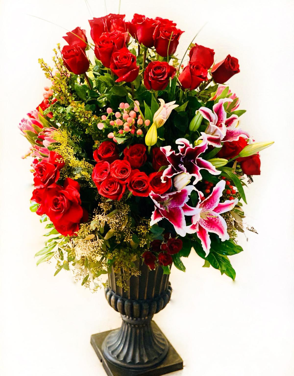 Tall arrangement of red roses and pink lilies in a dark pedestal vase