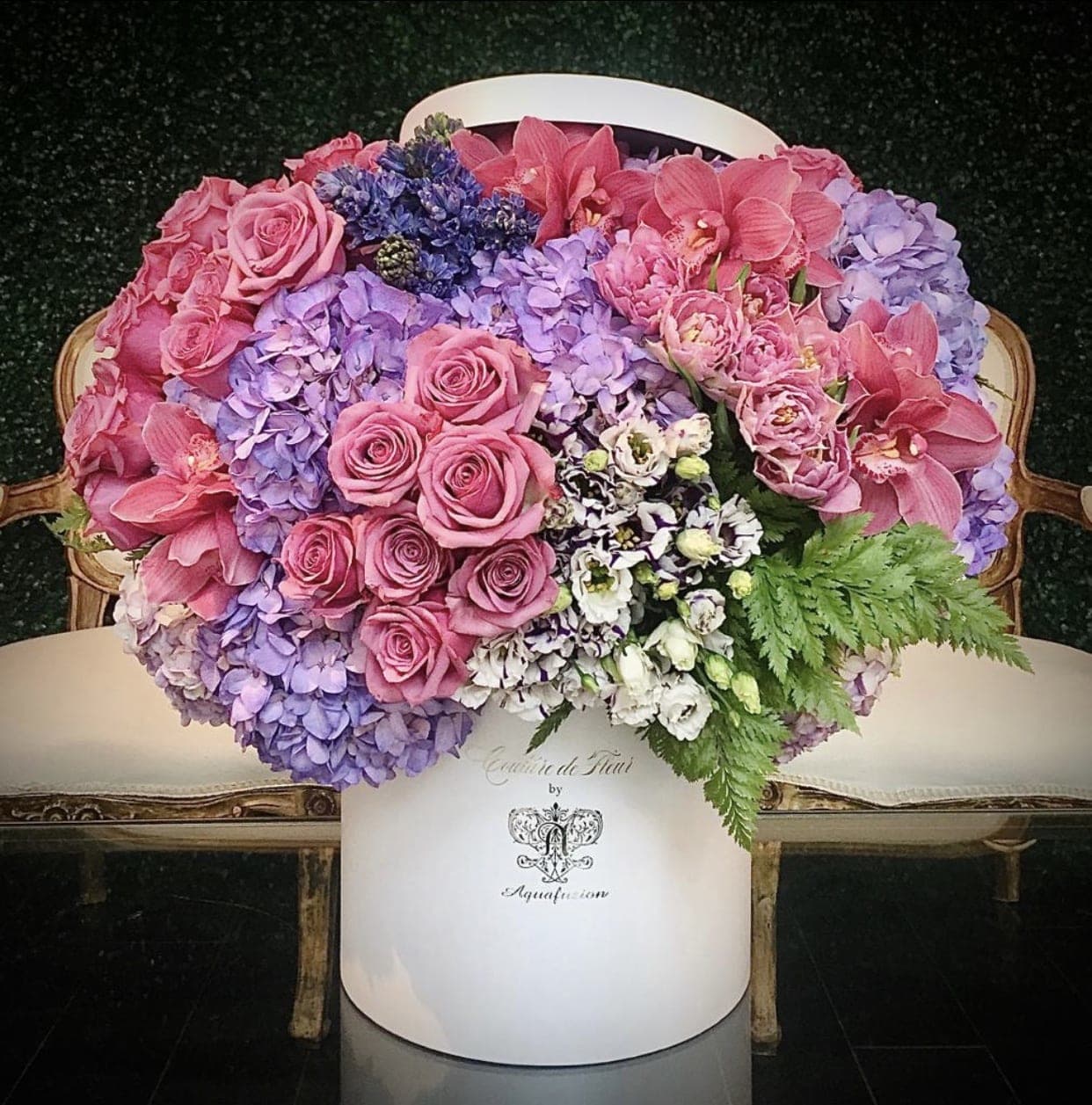 Pink roses and orchids arranged with lavender hydrangeas in a white hatbox