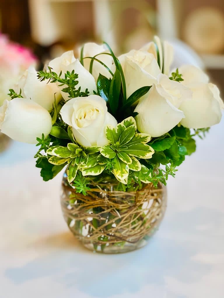 White roses arranged in a clear glass vase with green foliage