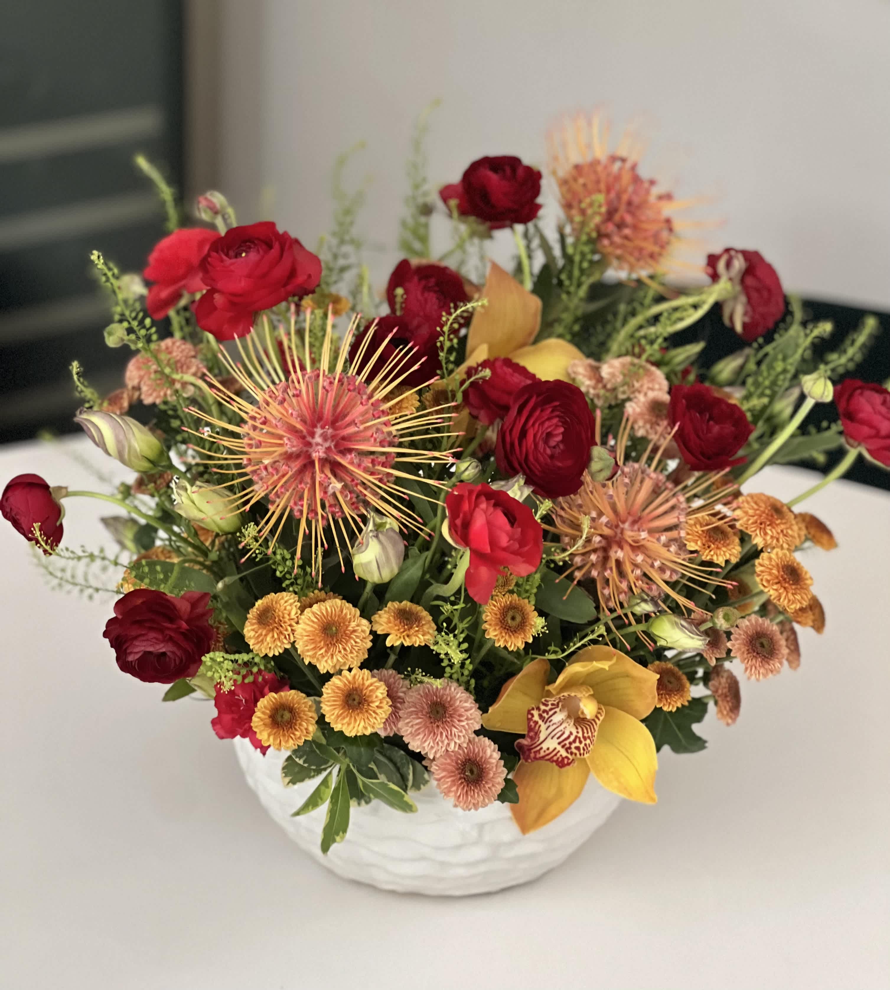 A Timeless Kaleidoscope - Discover elegance in every petal with our exquisite warm-toned floral arrangement. Immerse yourself in the rich hues of fall, showcased in unique blooms carefully curated to bring a touch of nature's beauty to your space. Presented in a ceramic vase, this arrangement is a harmonious blend of sophistication and charm. 