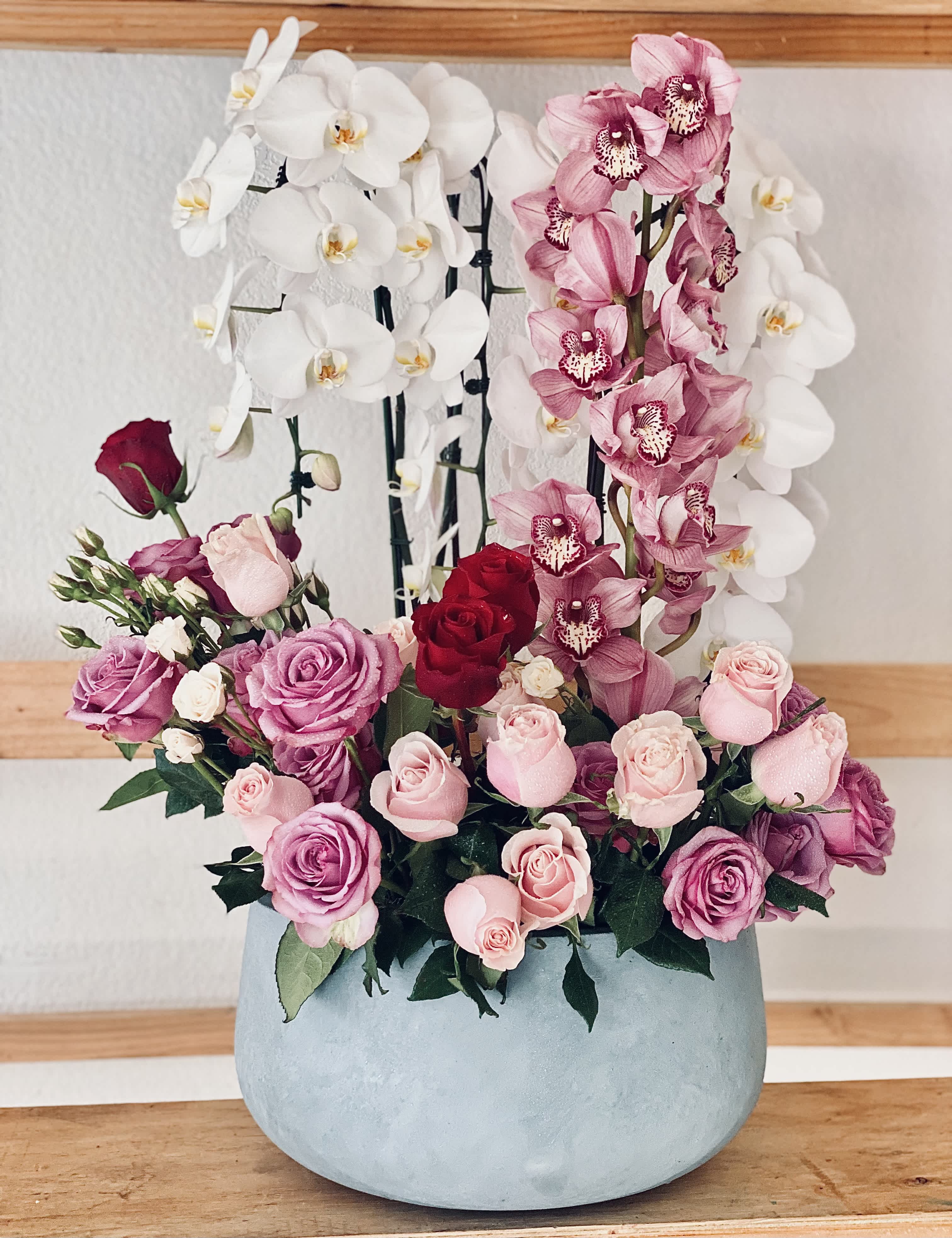 Pink and white orchids with roses in a round blue vase