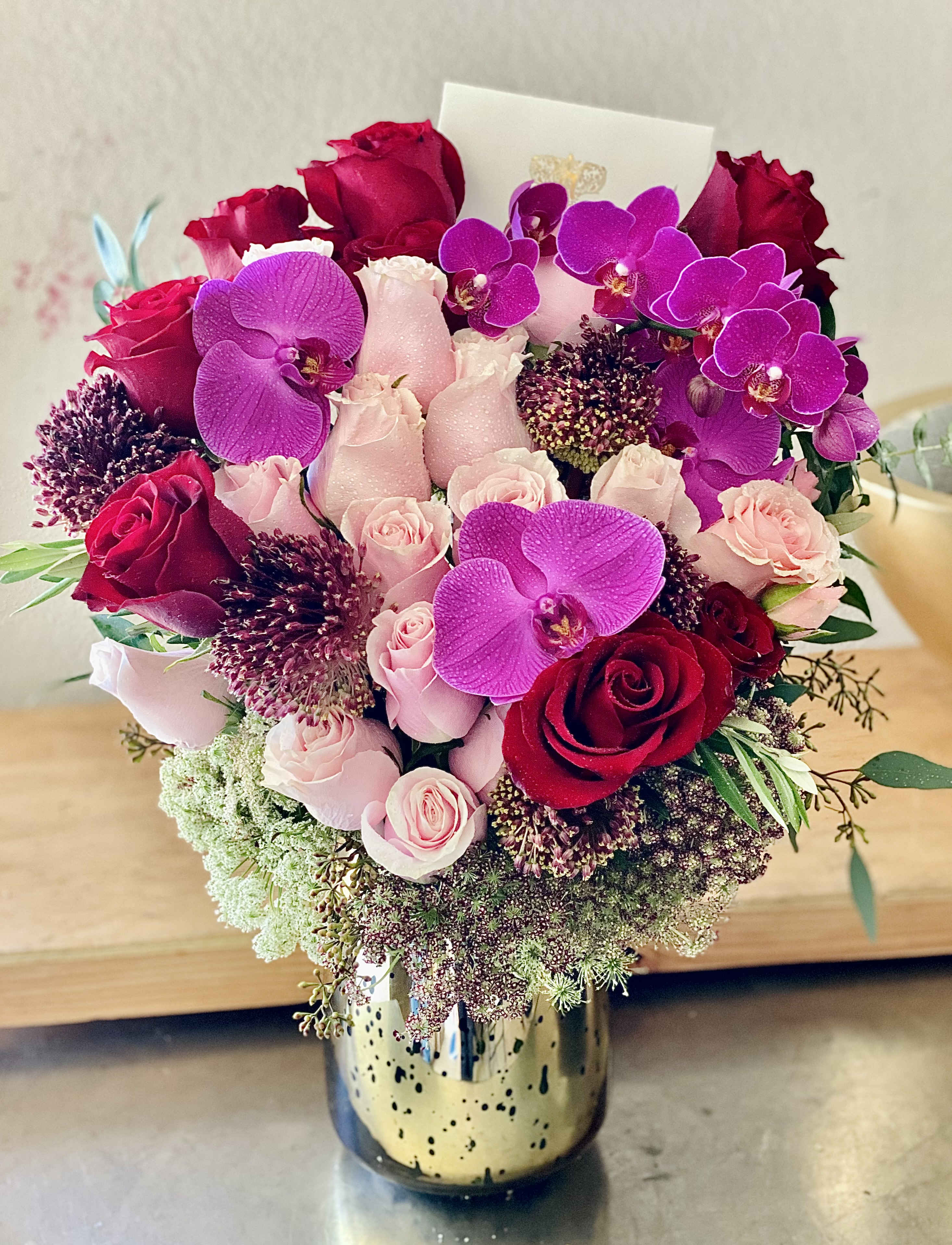 Bouquet of red and pink roses with purple orchids in a gold vase