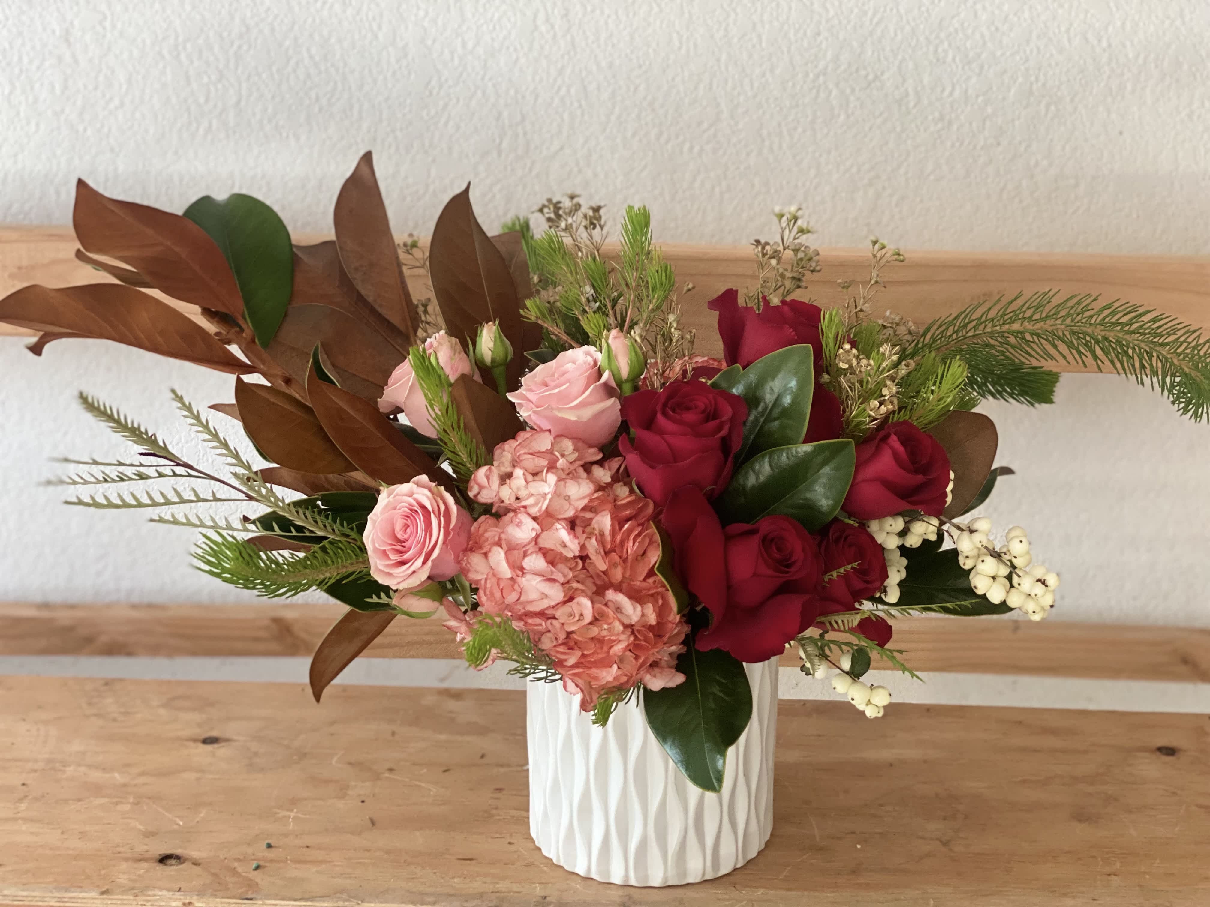 Pink and red roses in a white textured vase with mixed greenery