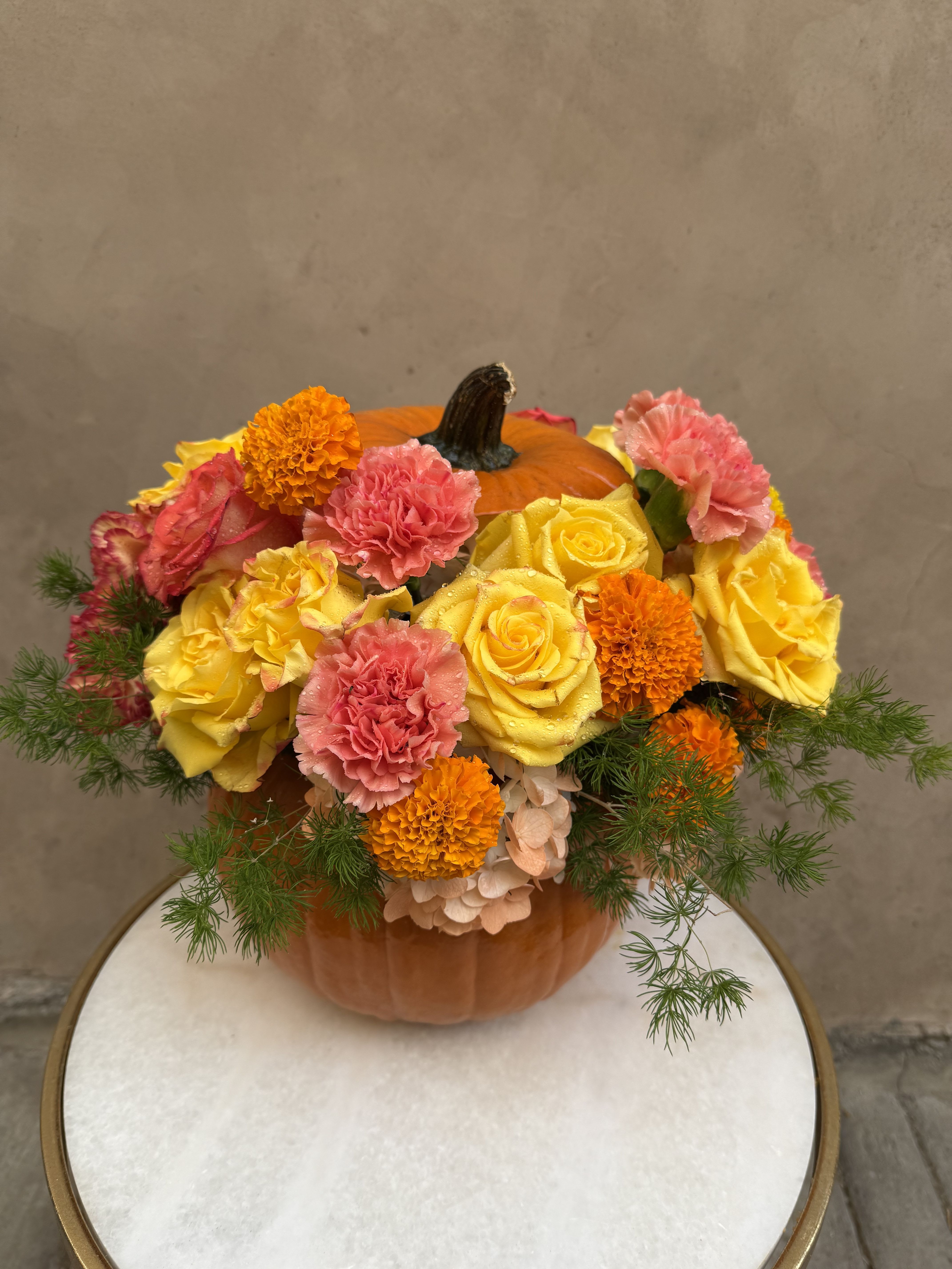 Pumpkin centerpiece with yellow roses, pink carnations, and orange marigolds