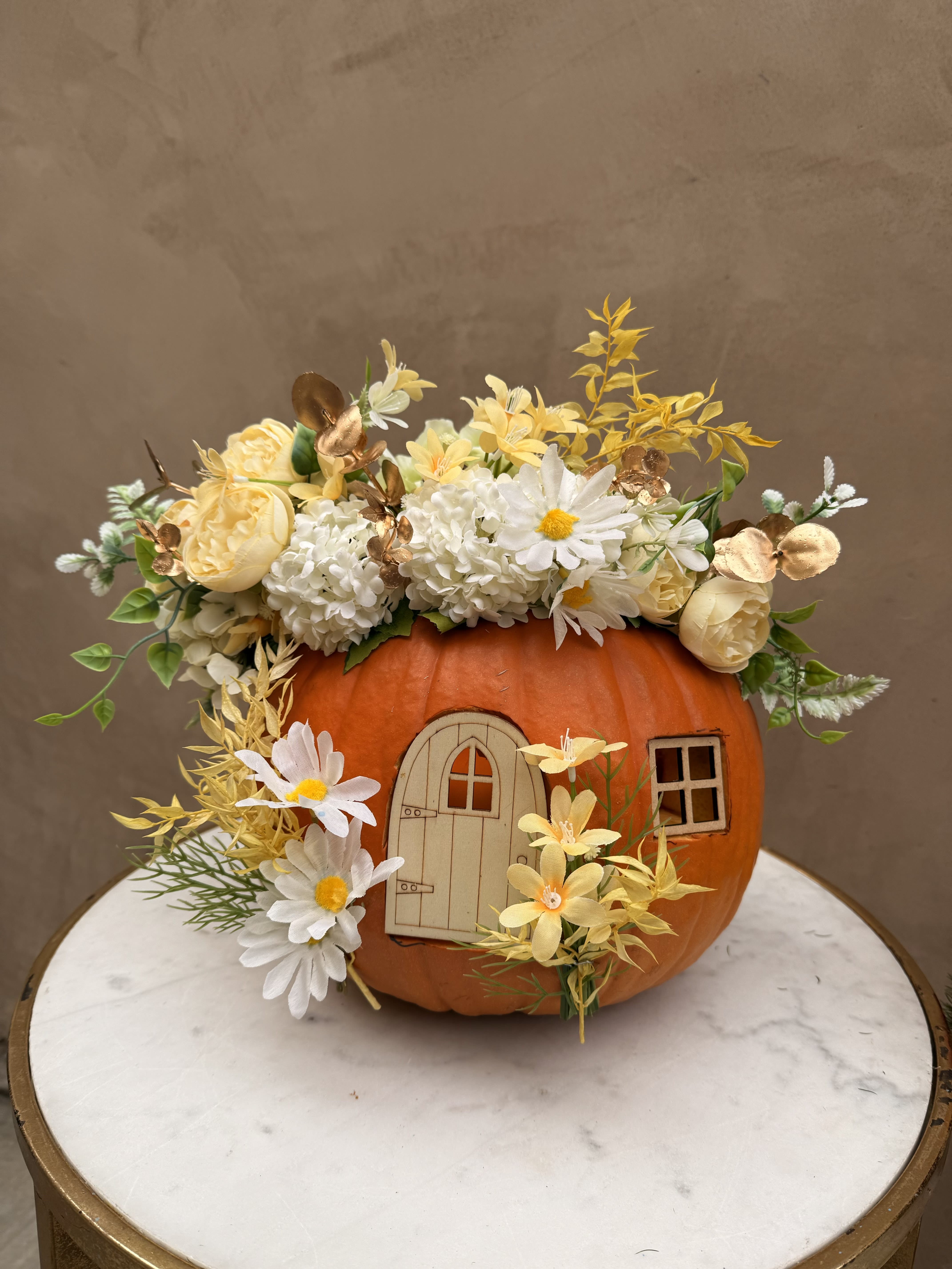 Pumpkin decorated with white and yellow flowers and a small door cutout