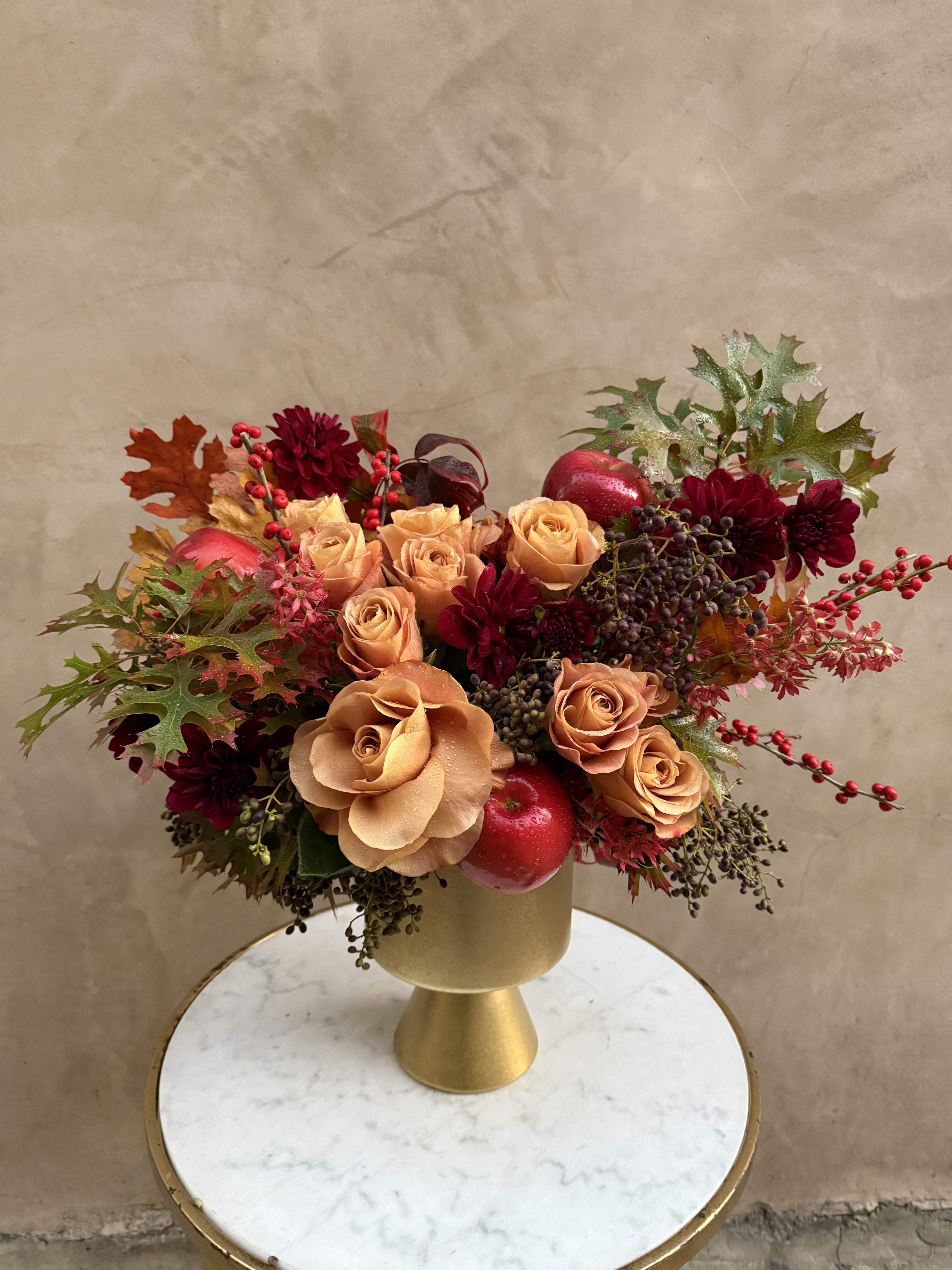 Peach roses and burgundy flowers in a gold vase with autumn leaves and berries