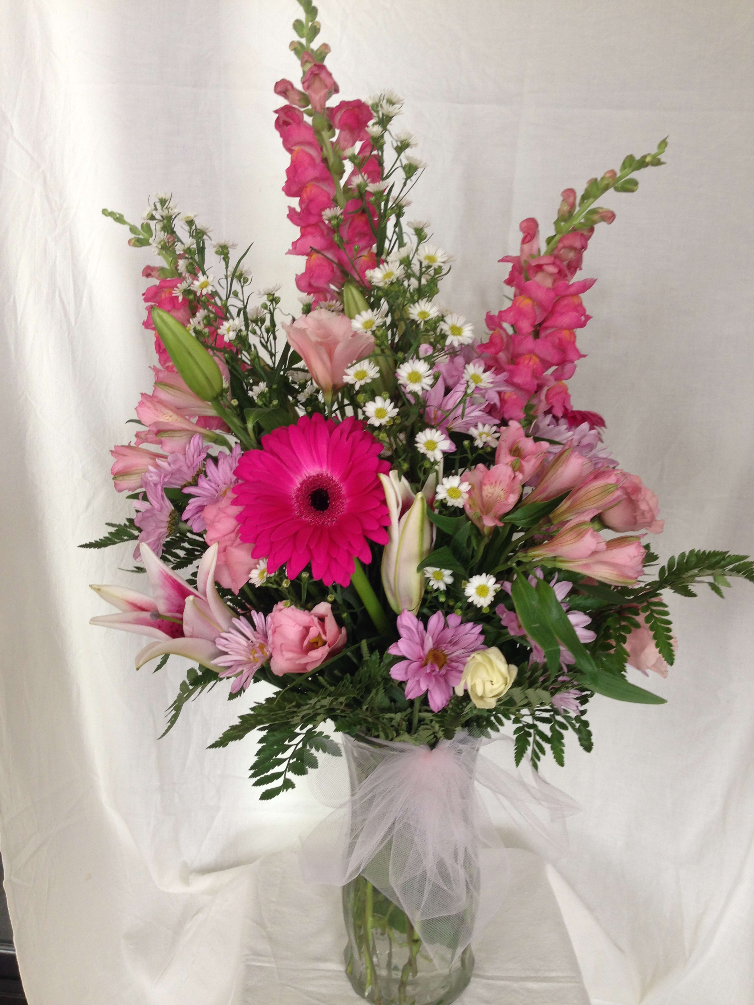 Pink mixed flower arrangement in a glass vase with a tulle bow